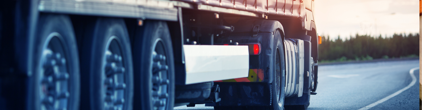 a scenic image of a navy lorry travelling down a main road underneath a pink and blue sky