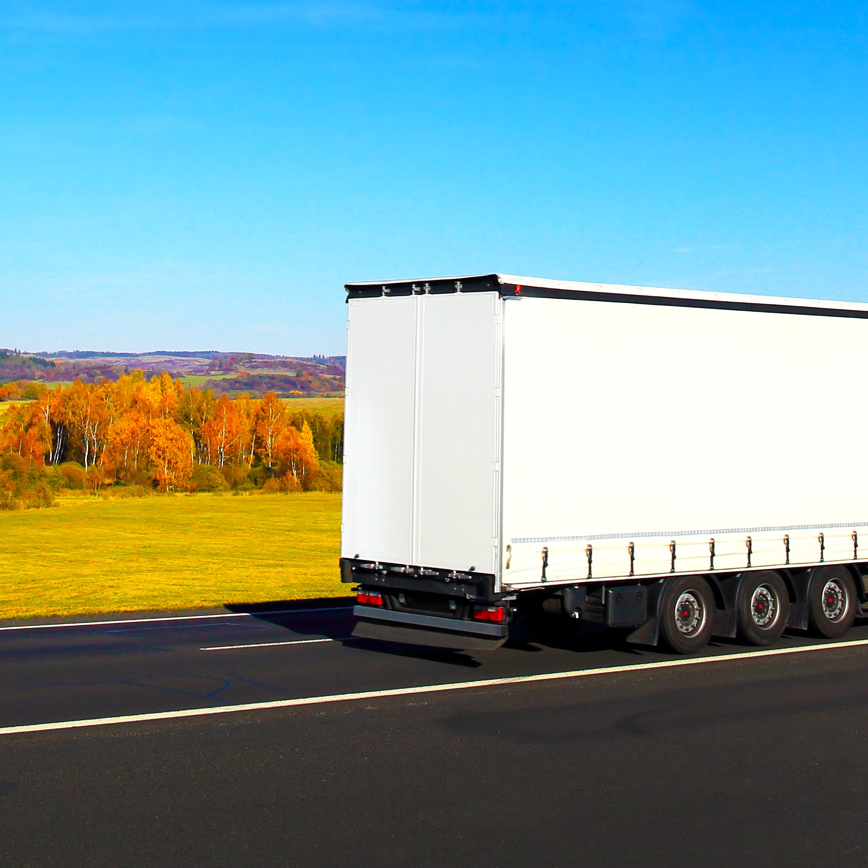 Red and white lorry driving along main road using taut straps 