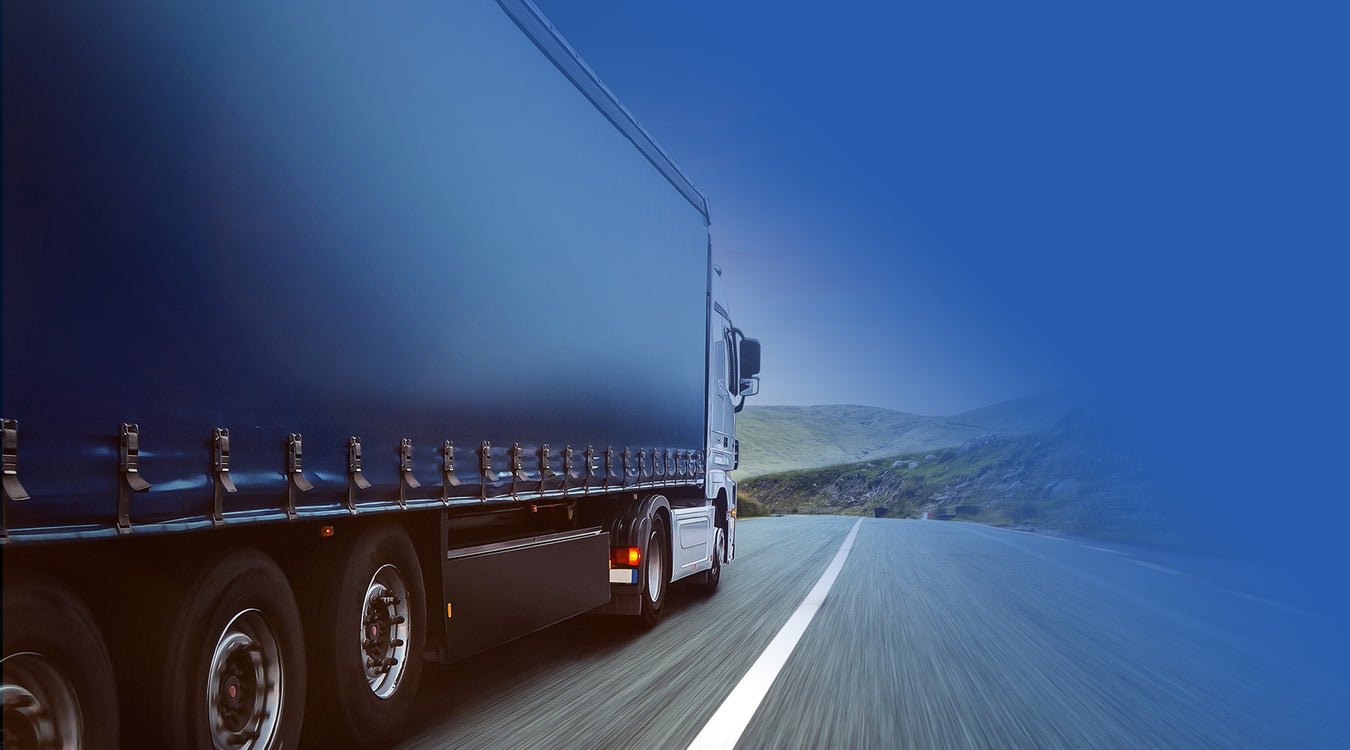 a large navy coloured lorry travelling on a main road with black taut straps attached to the sides